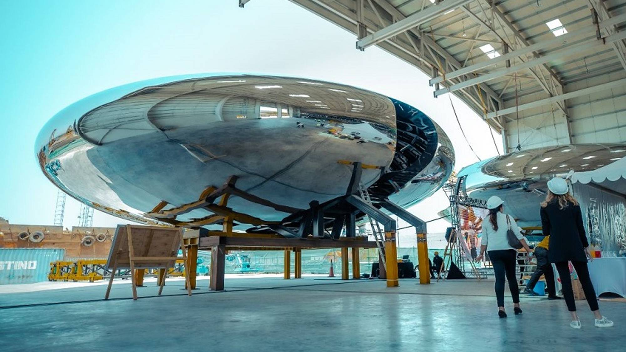 A pair of individuals standing before a massive metallic sphere, representing teamwork and solidarity